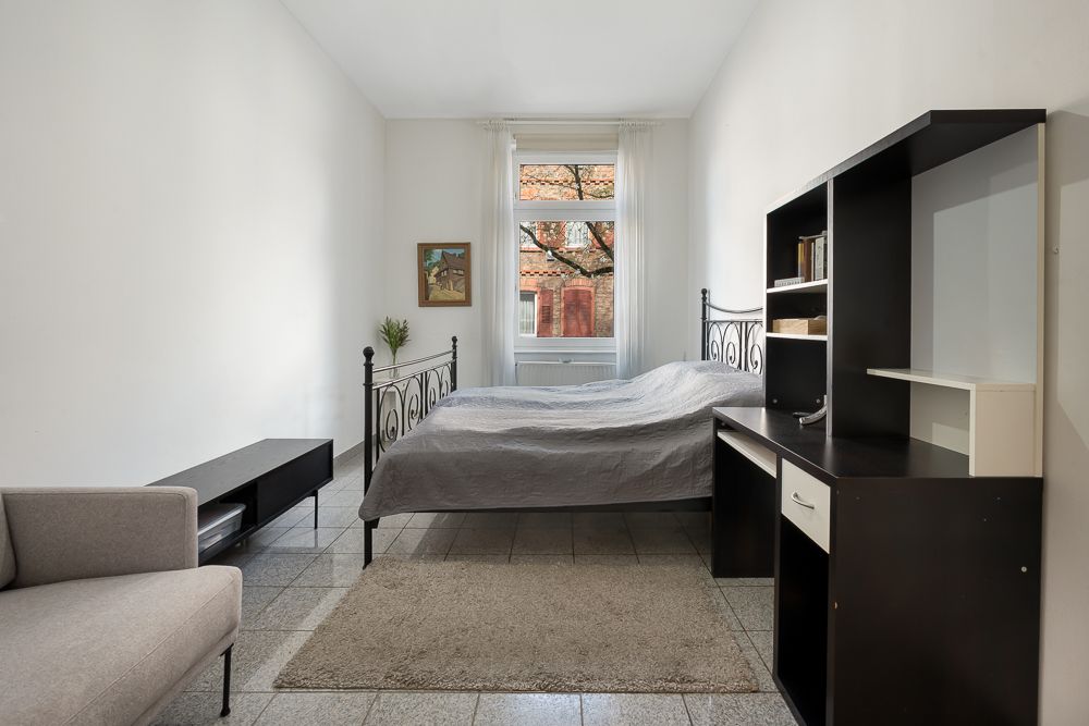 Schlafzimmer mit Bett, Schreibtisch, Regal, Sessel und Fenster mit Blick nach draußen.
