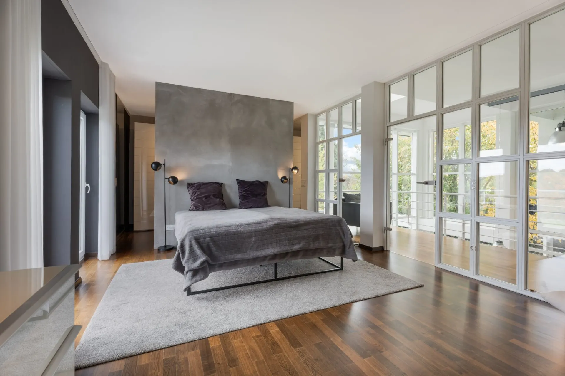 Modernes Schlafzimmer mit Doppelbett, Holzfußboden und großen Fenstern.
