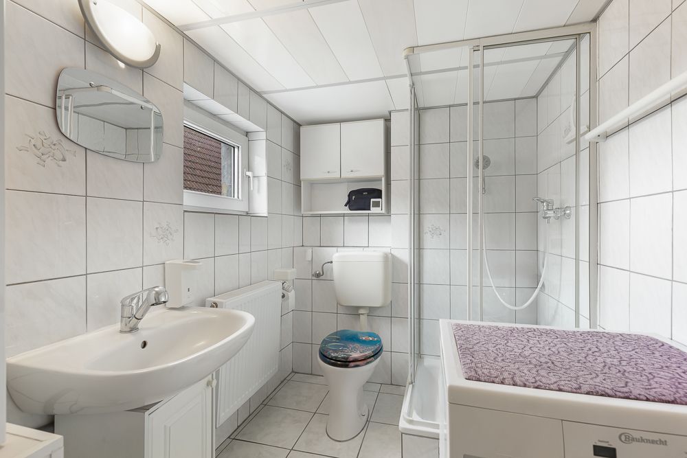Helles Badezimmer mit Waschbecken, Toilette, Dusche und Waschmaschine.