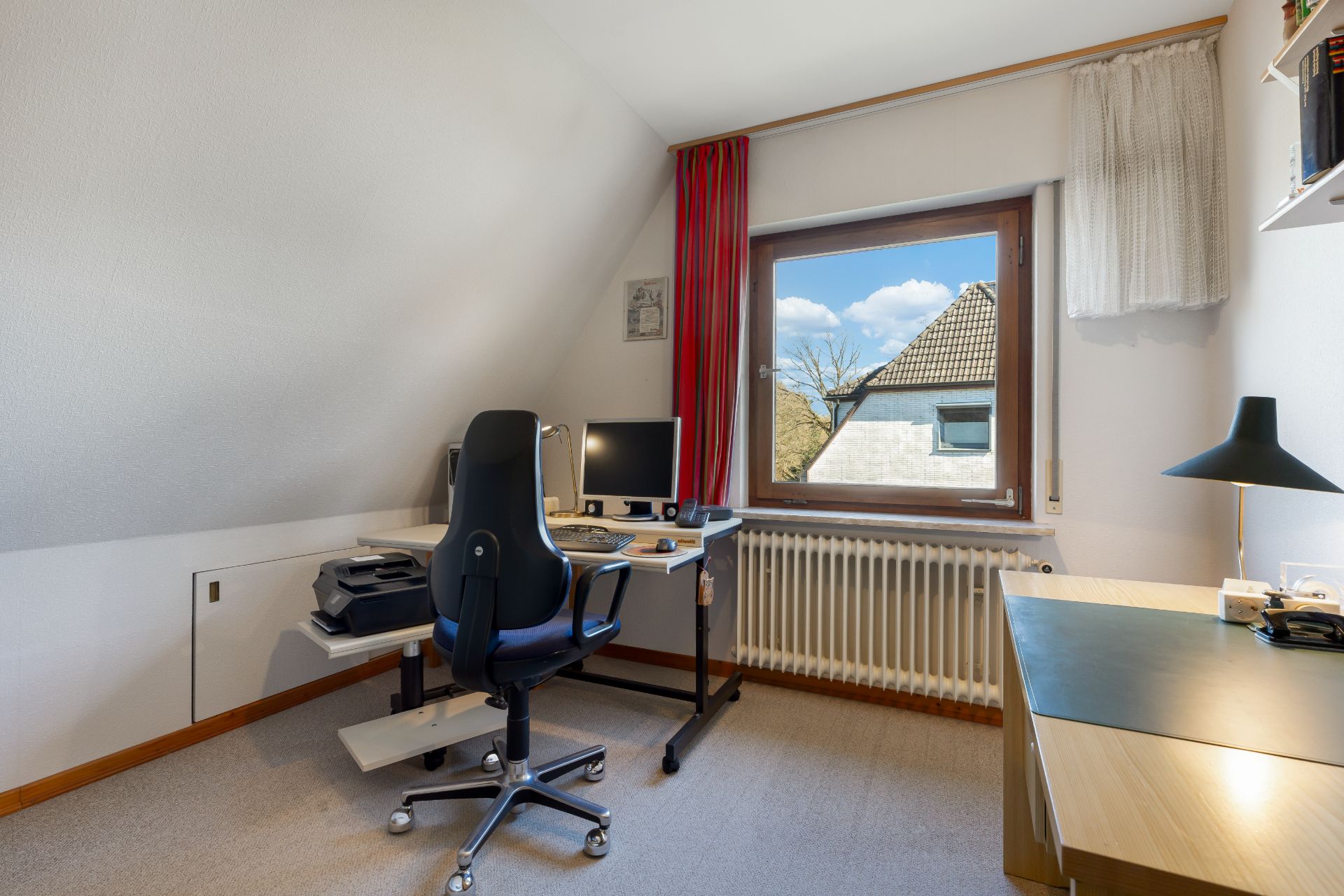 Helles Arbeitszimmer mit Schreibtisch, Stuhl, Computer und großem Fenster mit Blick nach draußen.