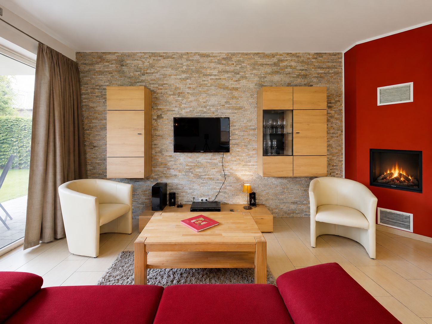 Modernes Wohnzimmer mit Kamin, zwei Sesseln, rotem Sofa, Couchtisch und TV an der Wand.