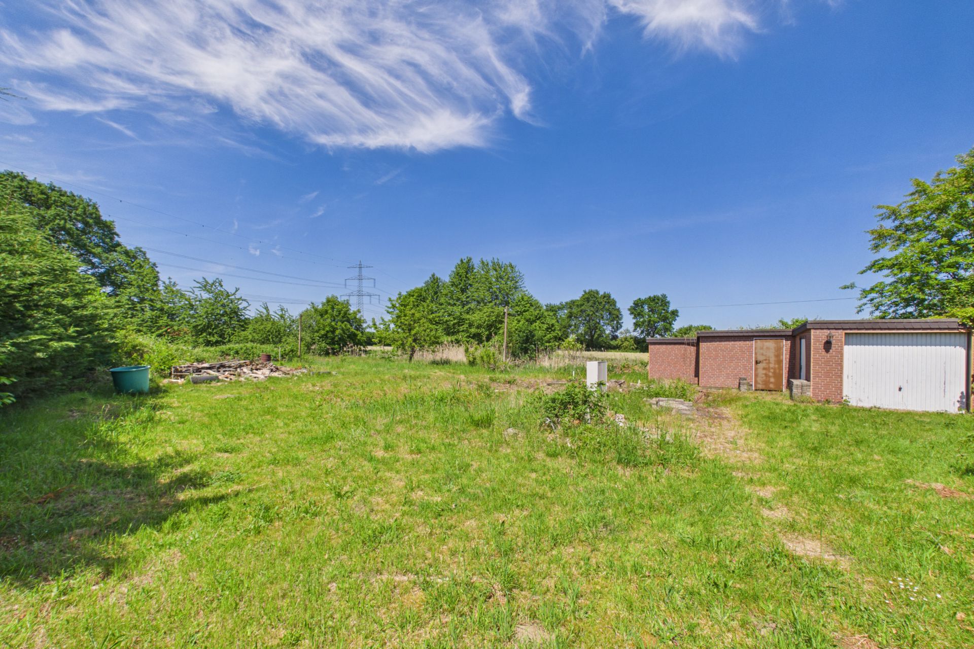 Großer, grüner Garten mit Rasen, Bäumen und einer Garage aus Backstein bei klarem Himmel.