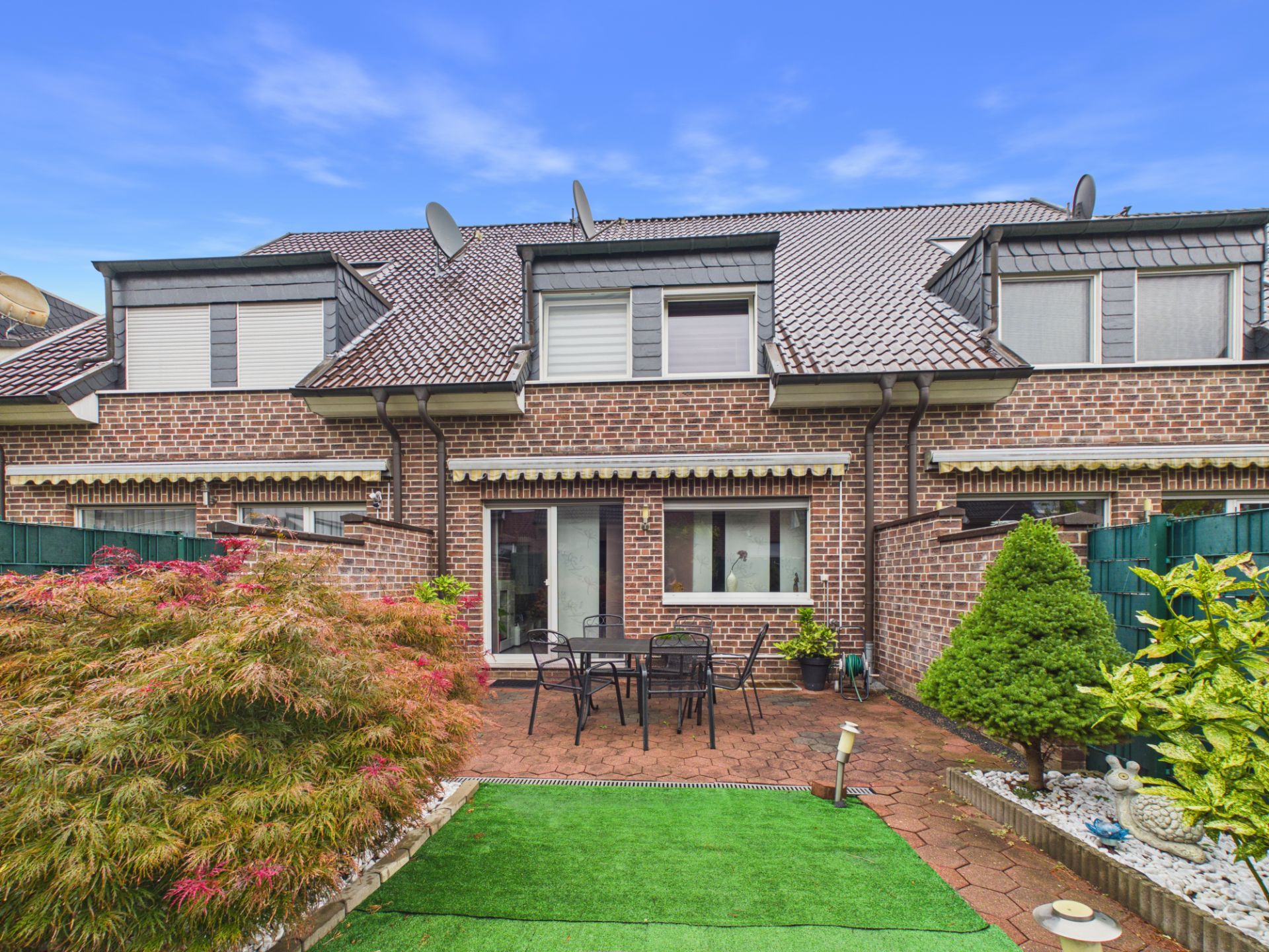 Gepflegter Hinterhof mit Terrasse, Gartenmöbeln, Pflanzen und Zugang zu einem Backsteinhaus.
