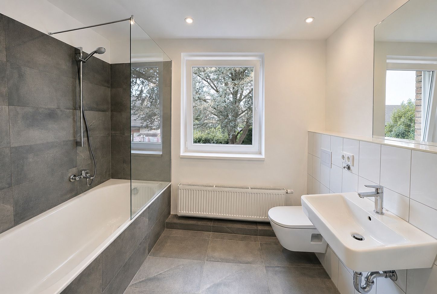 Modernes Bad mit Badewanne, Dusche, Waschbecken, WC und Fenster, graue Fliesen.