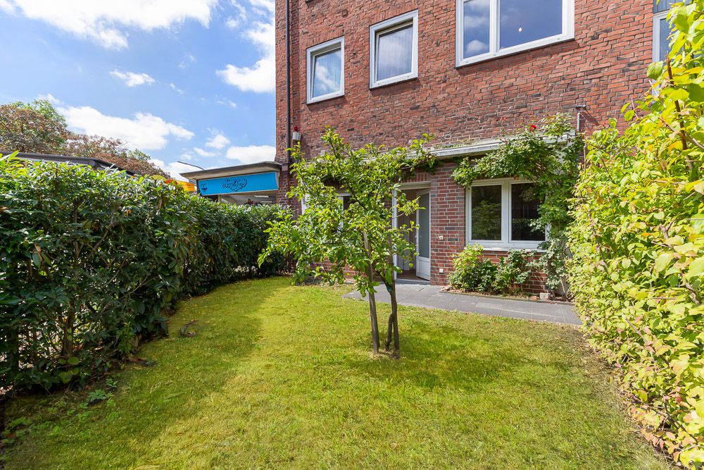 Kleiner Garten mit Rasen, Baum und Hecke vor einem Backsteinhaus mit Fenstern.