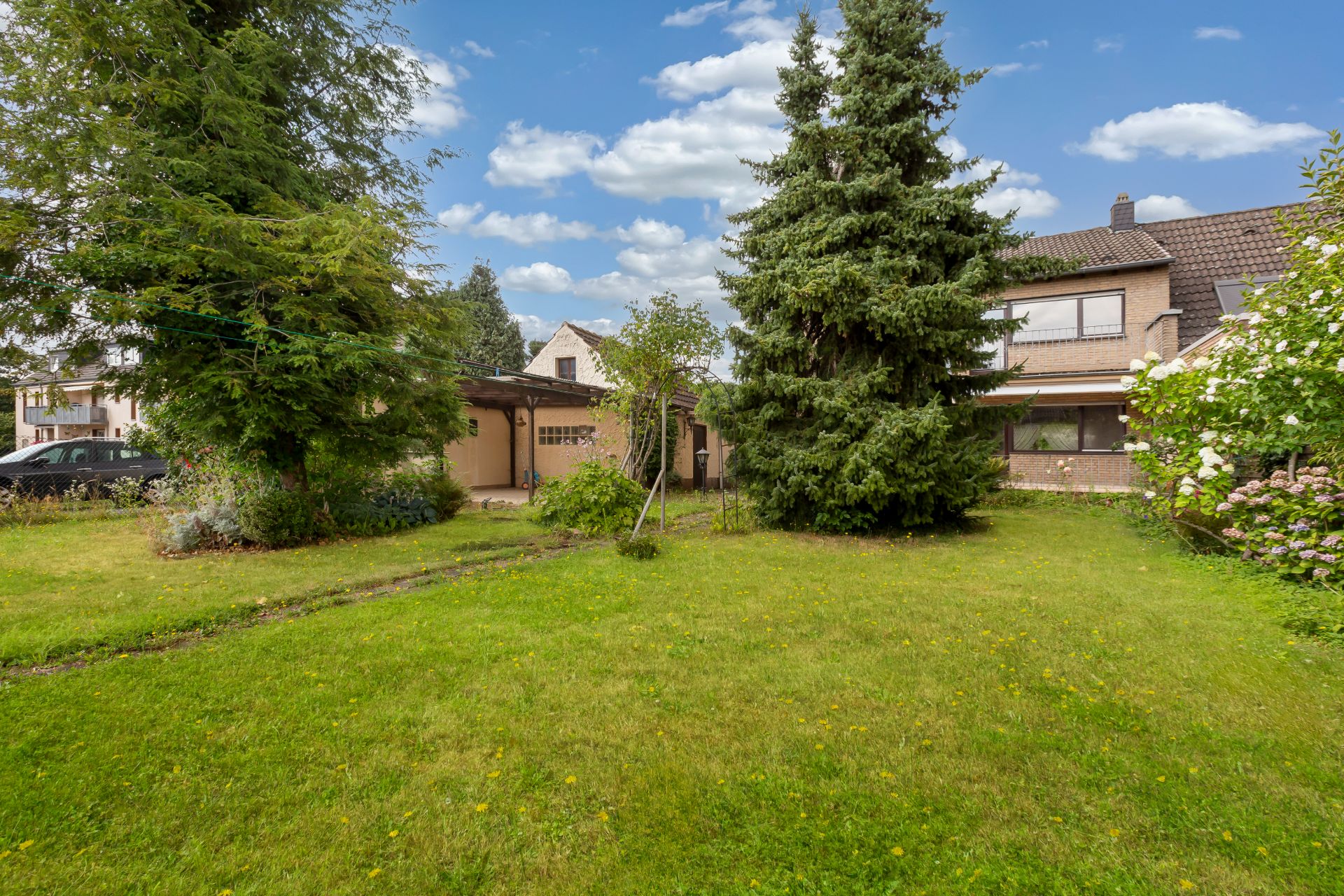 Großer Garten mit Rasenfläche, Bäumen und Sträuchern hinter einem Wohnhaus.