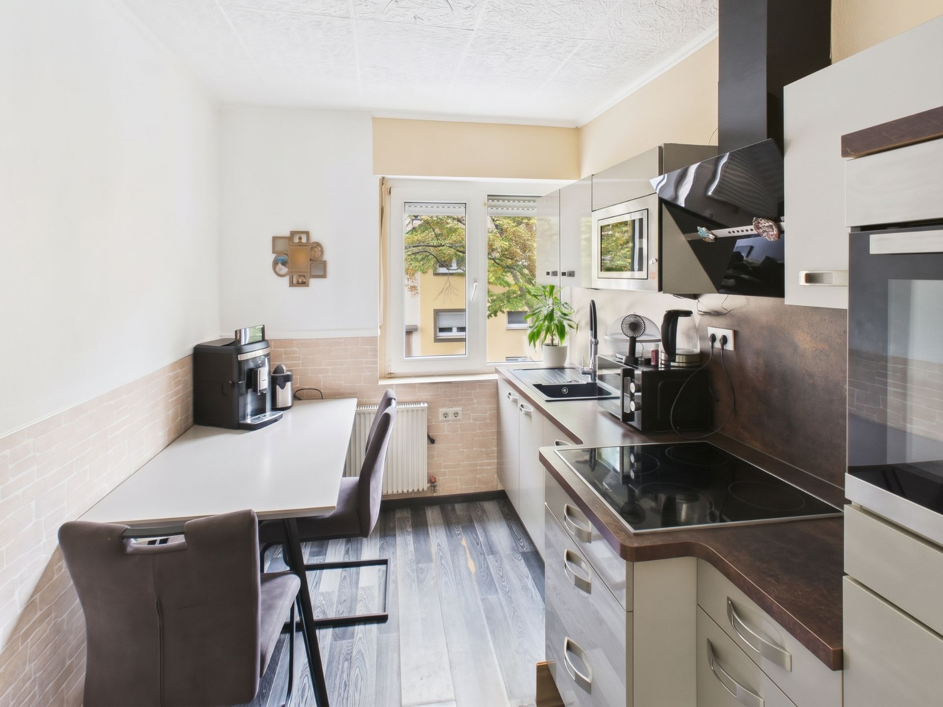Helle, moderne Küche mit Esstisch, Kochfeld, Einbaugeräten und Fenster mit Blick nach draußen.