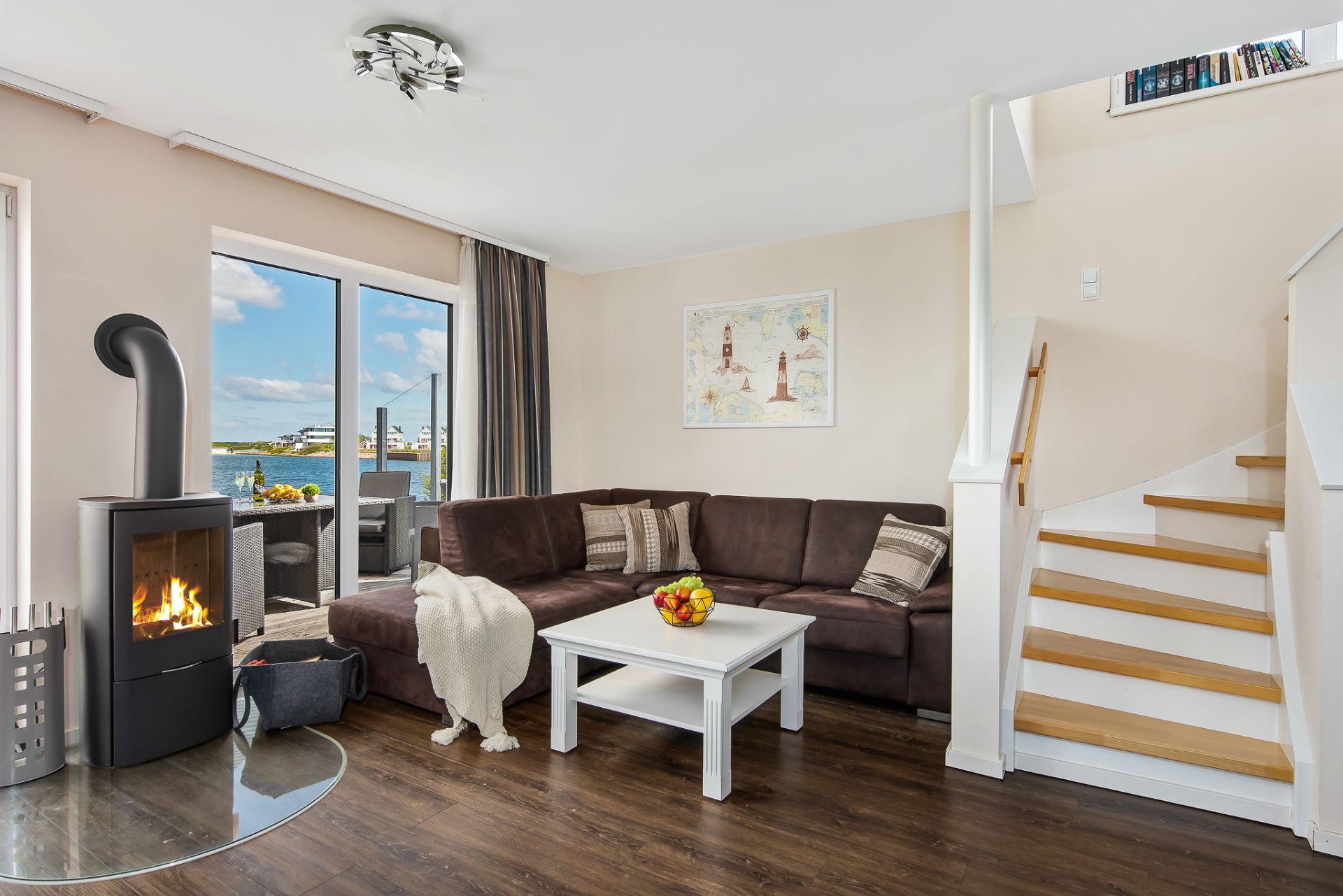 Wohnzimmer mit braunem Sofa, Kamin, weißem Tisch, Treppe und Ausblick nach draußen.