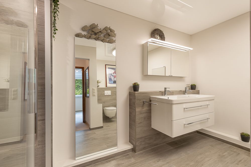 Modernes Badezimmer mit großem Spiegel, Waschbecken und grau-weißer Einrichtung.