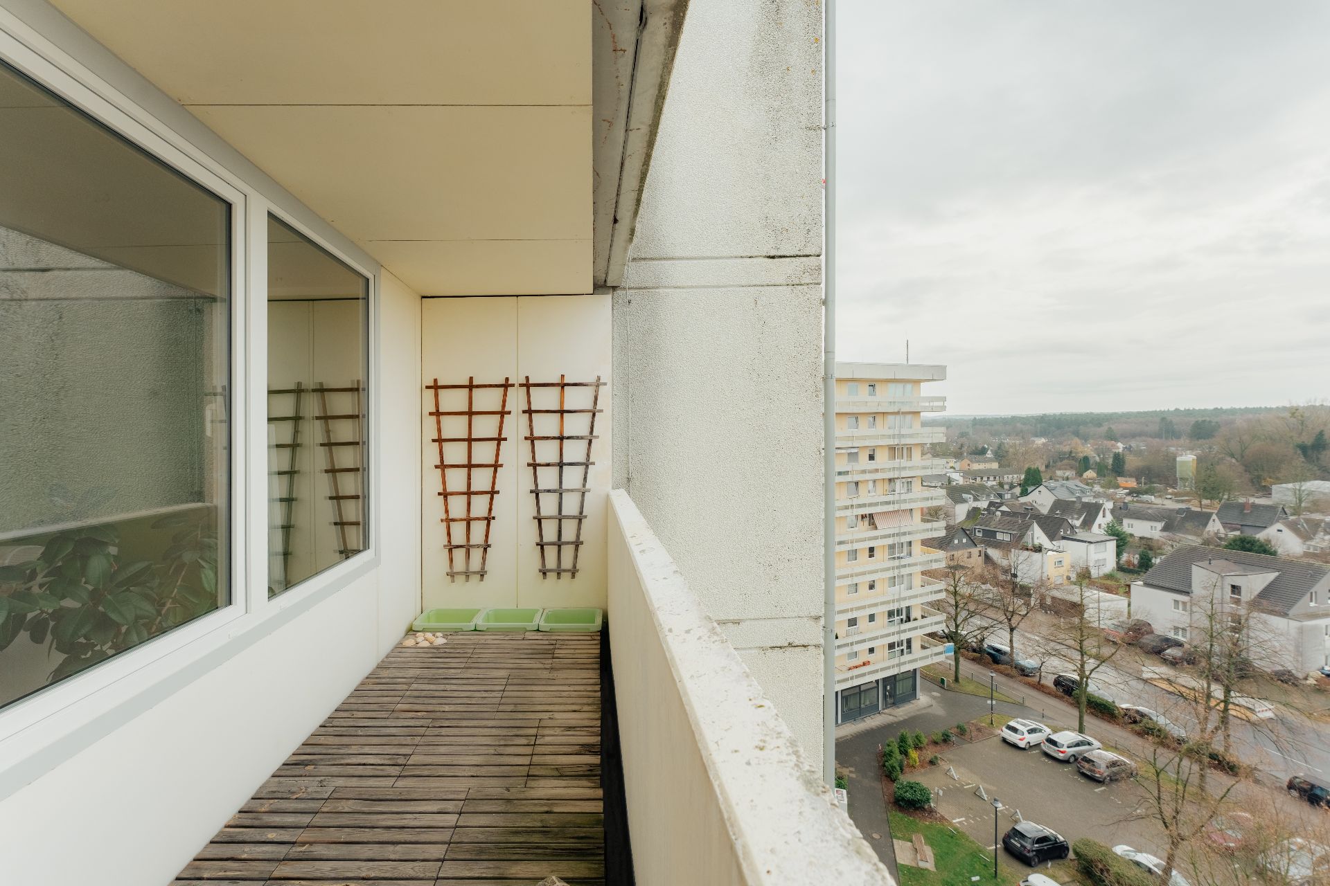 Balkon mit Holzfußboden, zwei Rankgittern und Blick auf Wohngebiet.