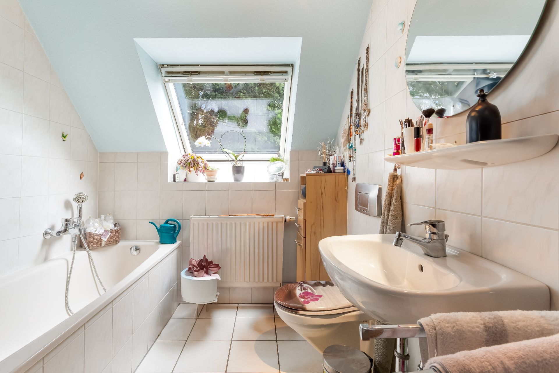 Helles Badezimmer mit Badewanne, Waschbecken, Toilette und Dachfenster mit Pflanzen.