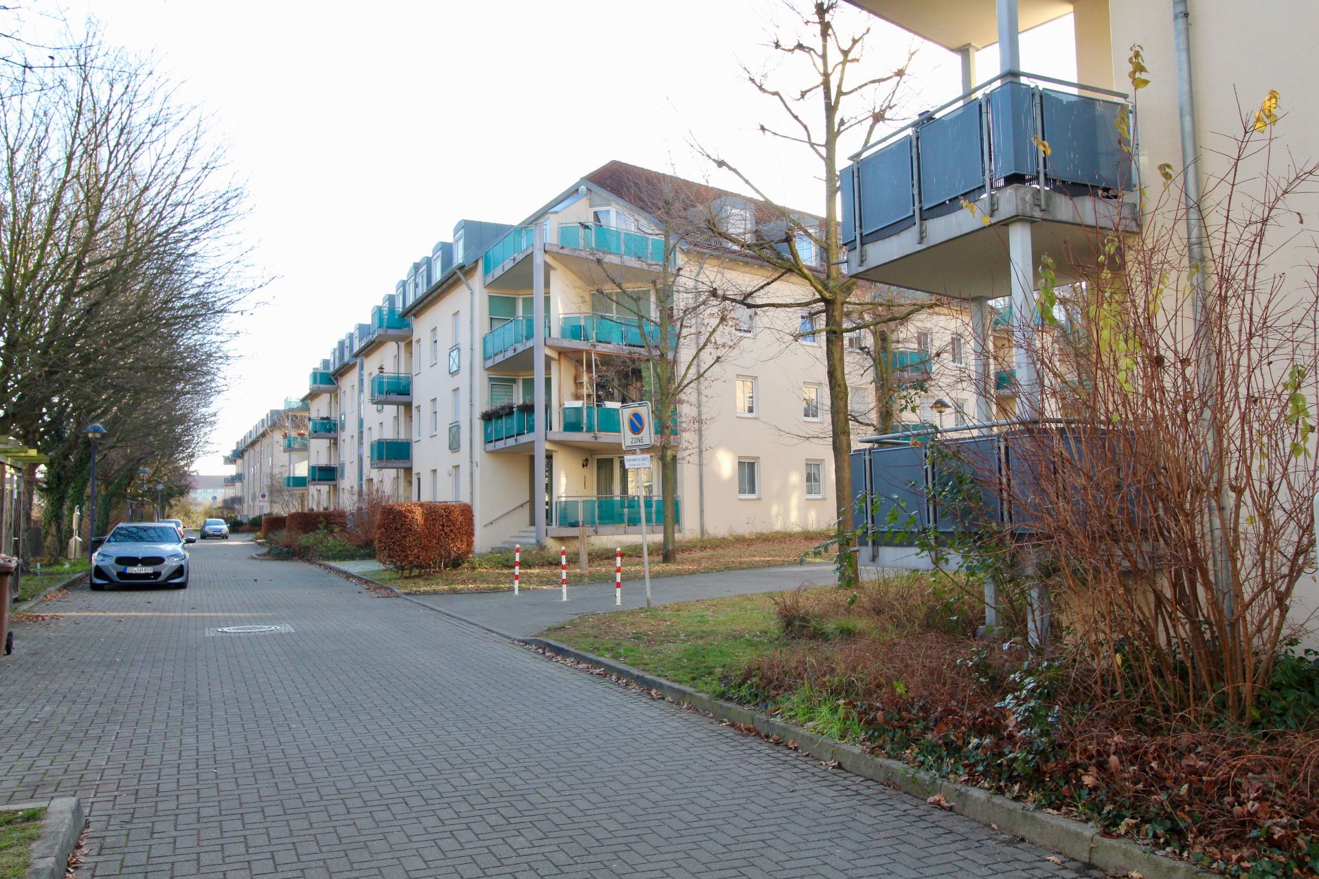 Mehrstöckige Wohngebäude mit Balkonen an einer ruhigen Straße, wenige Autos und Bäume im Winter.