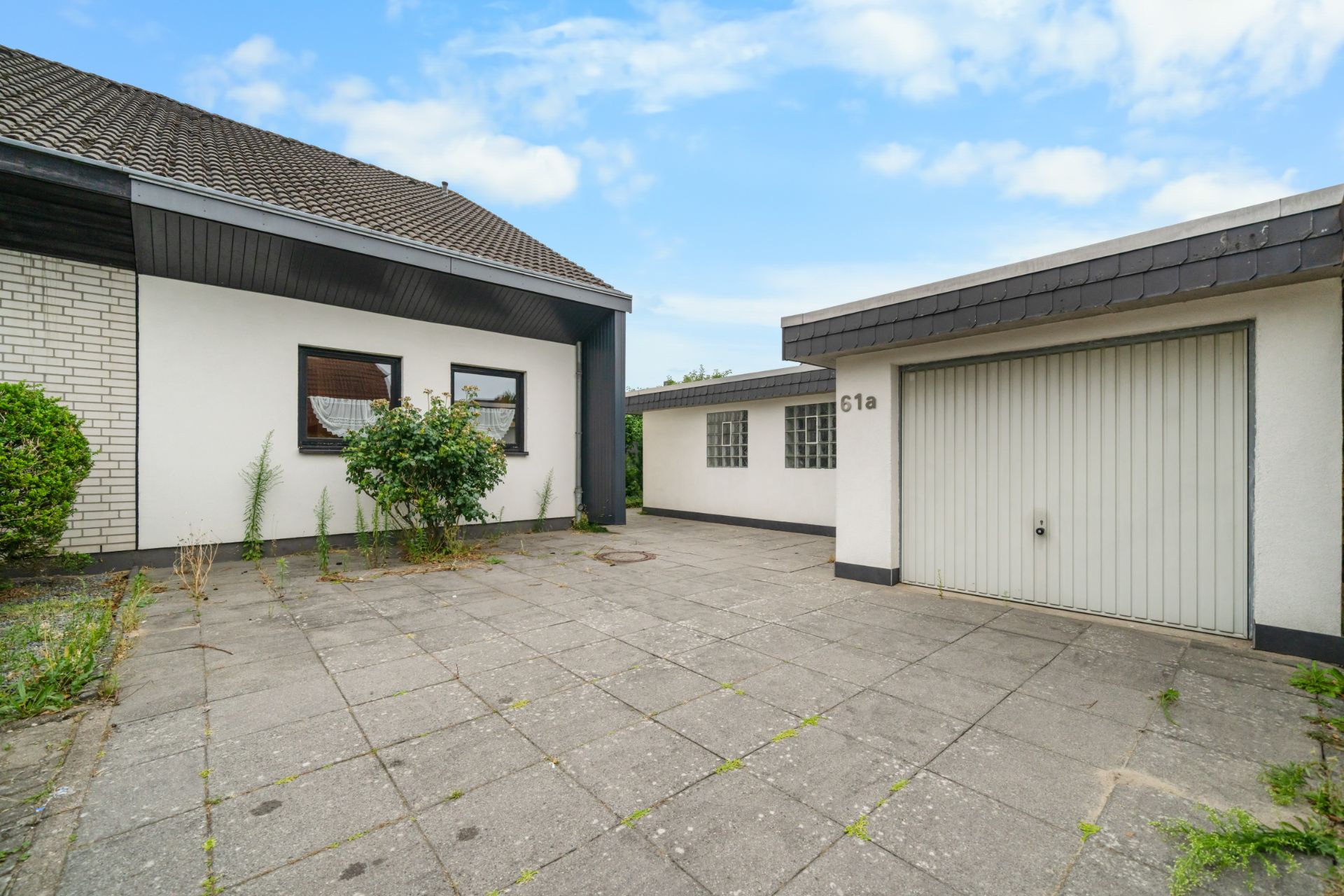Gepflasterter Hof mit Garage und Haus, gestrichene weiße Wände, einige Pflanzen am Rand.