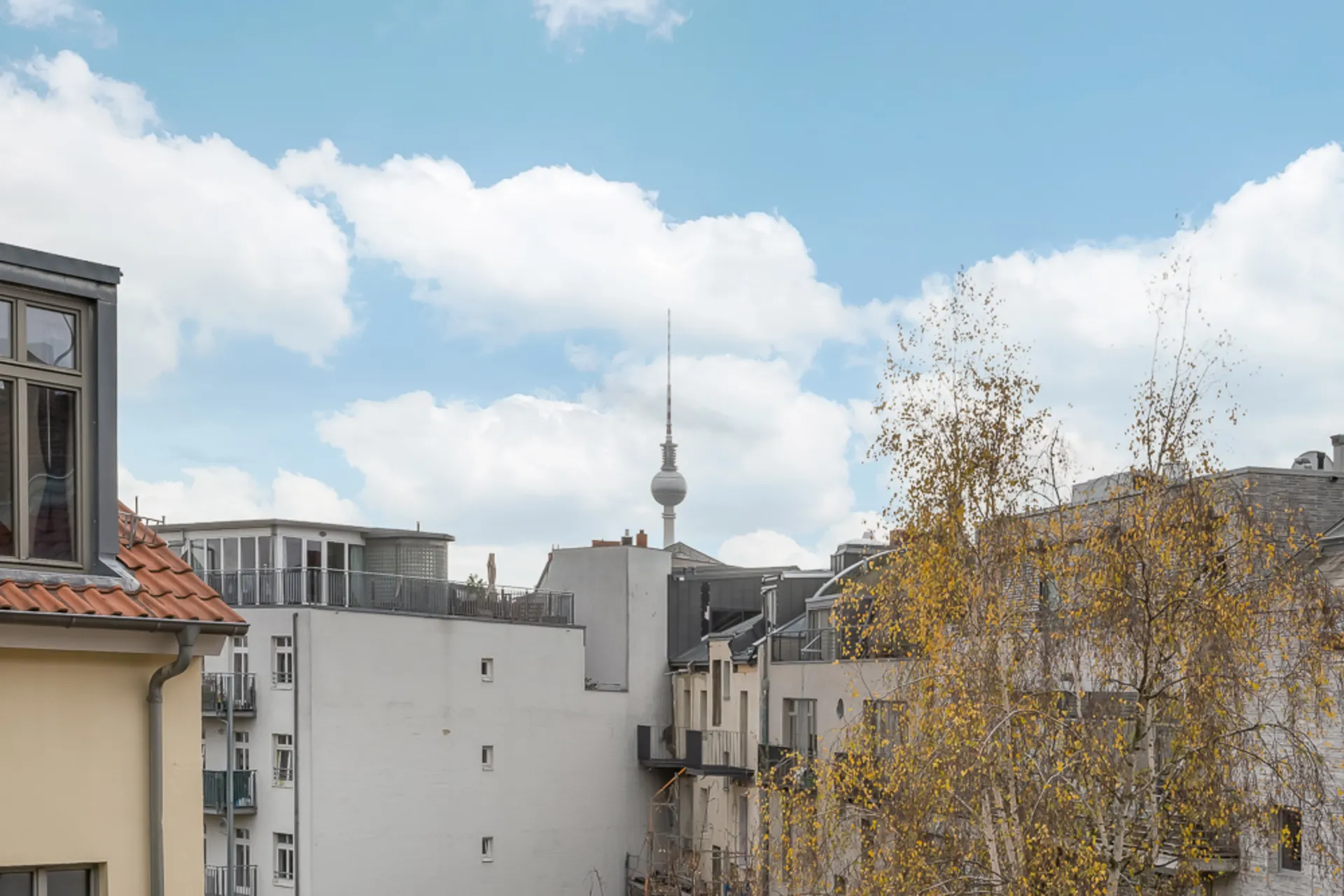 Blick von einem Balkon auf Wohngebäude mit Fernsehturm im Hintergrund und blauem Himmel.