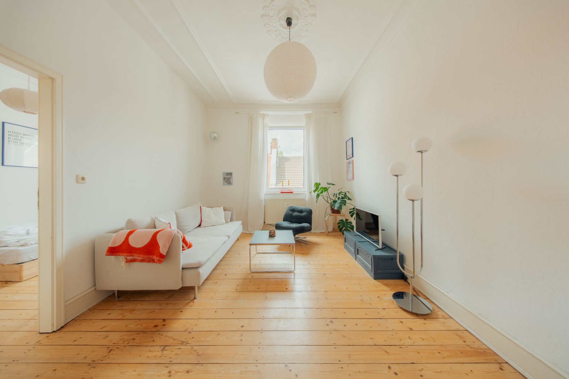 Helles Wohnzimmer mit Holzboden, Sofa, Sessel, Couchtisch, Fernseher und Stehlampe.