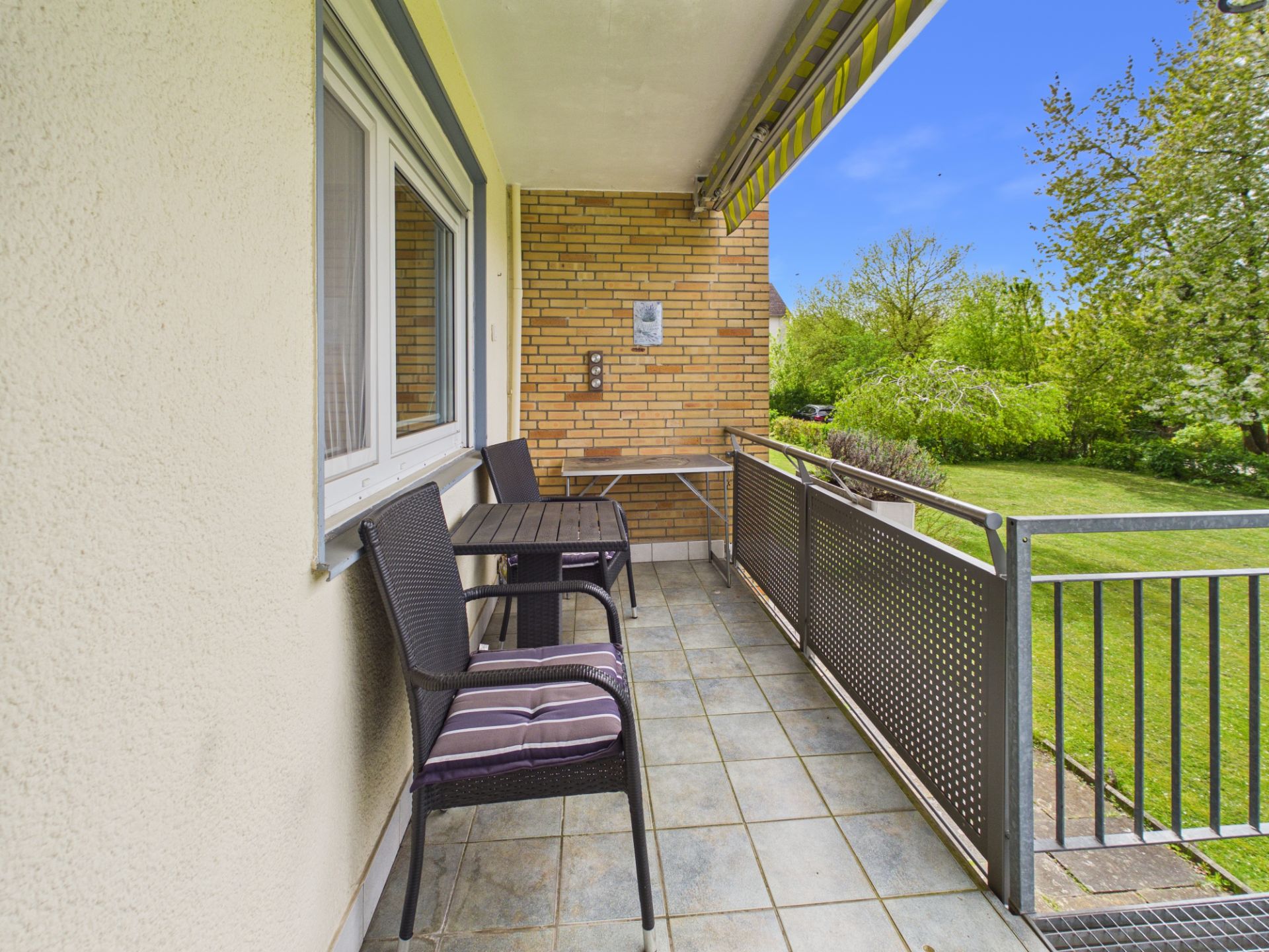 Balkon mit zwei Stühlen, Tisch, Markise und Blick auf grünen Garten.