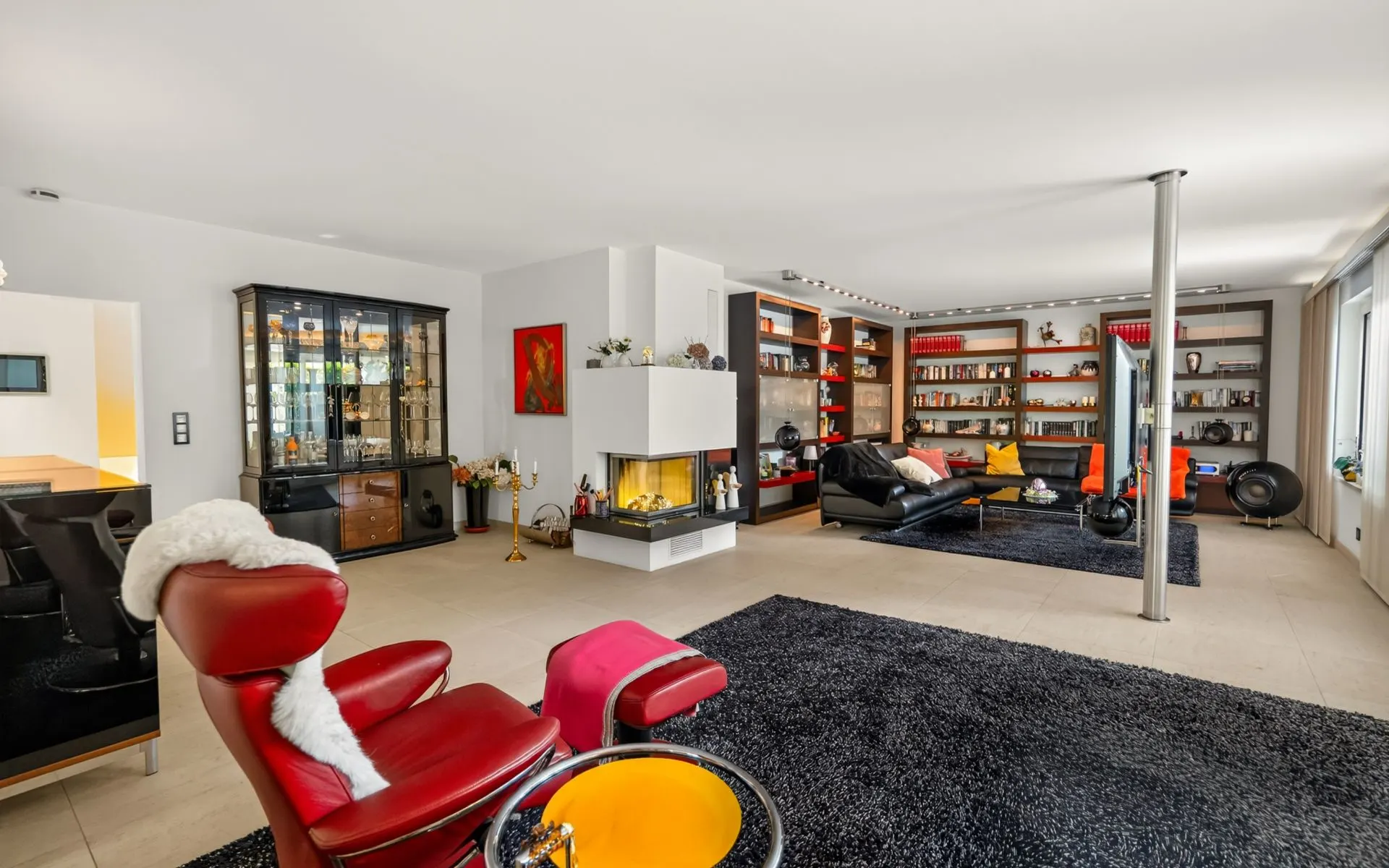 Modernes Wohnzimmer mit Kamin, roten Sesseln, Regalen und großen Teppichen.