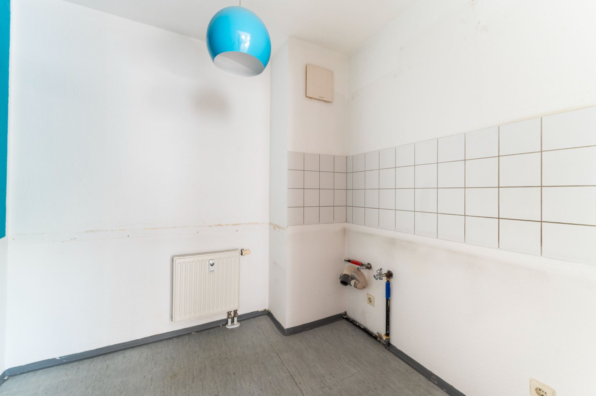 Leerer Raum mit weißen Wänden, Fliesenspiegel und blauer Lampe an der Decke.