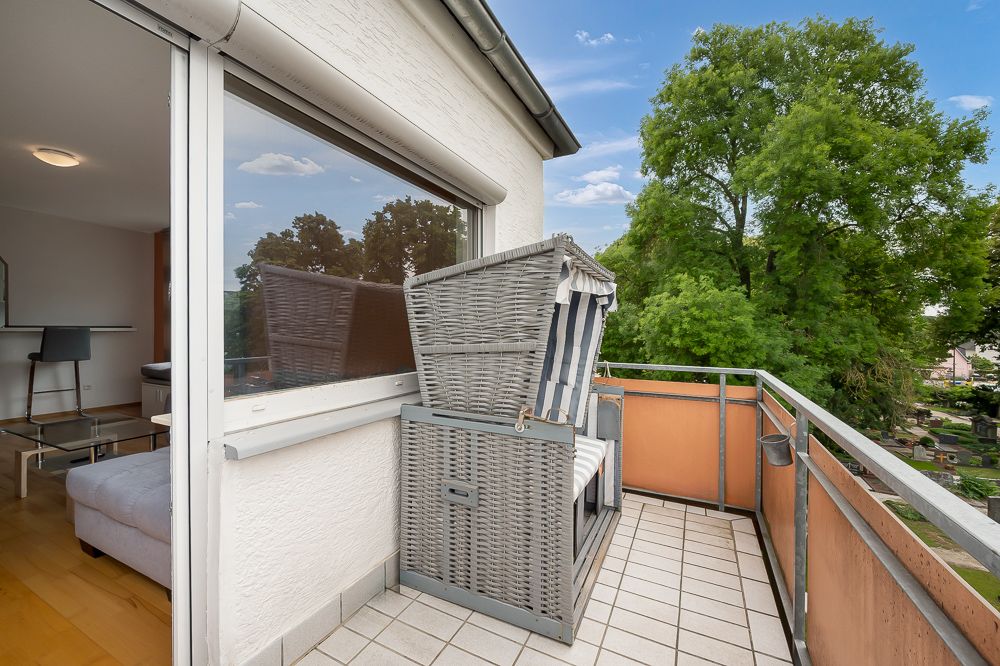 Balkon mit gefliestem Boden und einem Strandkorb, Blick ins Grüne.