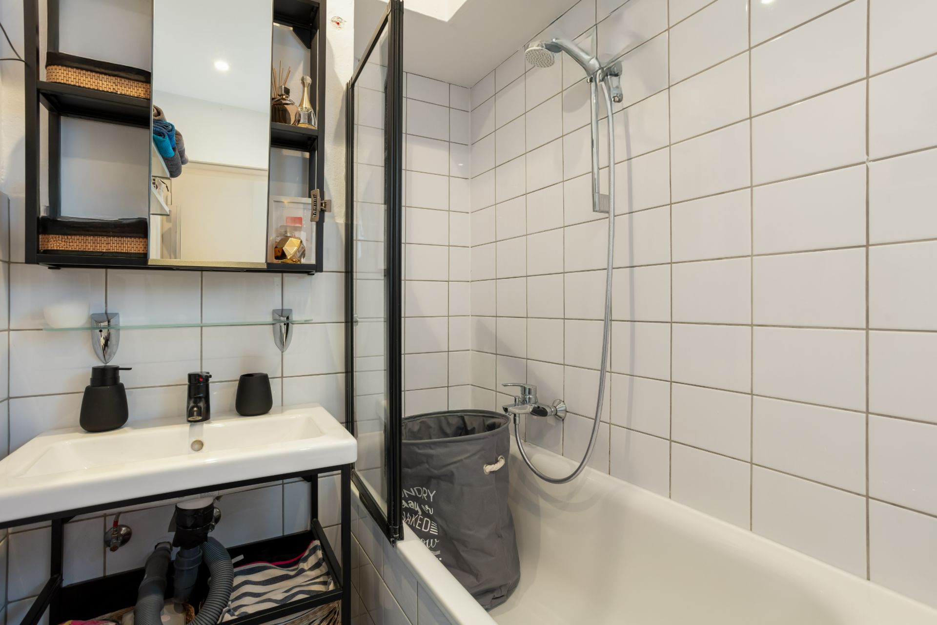 Modernes Badezimmer mit weiß gefliester Badewanne, Waschbecken und offenem Regal.