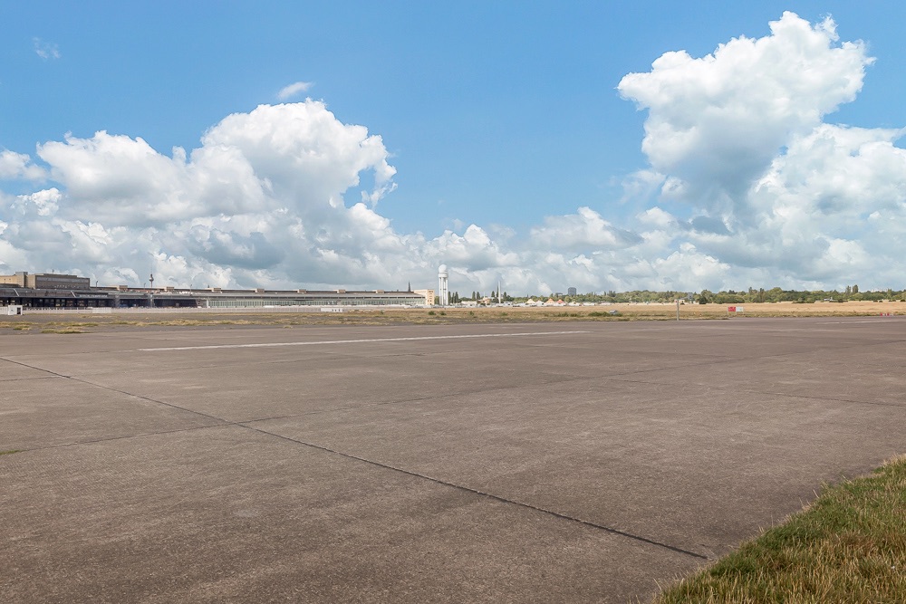 Große, leere Betonfläche im Freien mit etwas Gras und blauem Himmel.