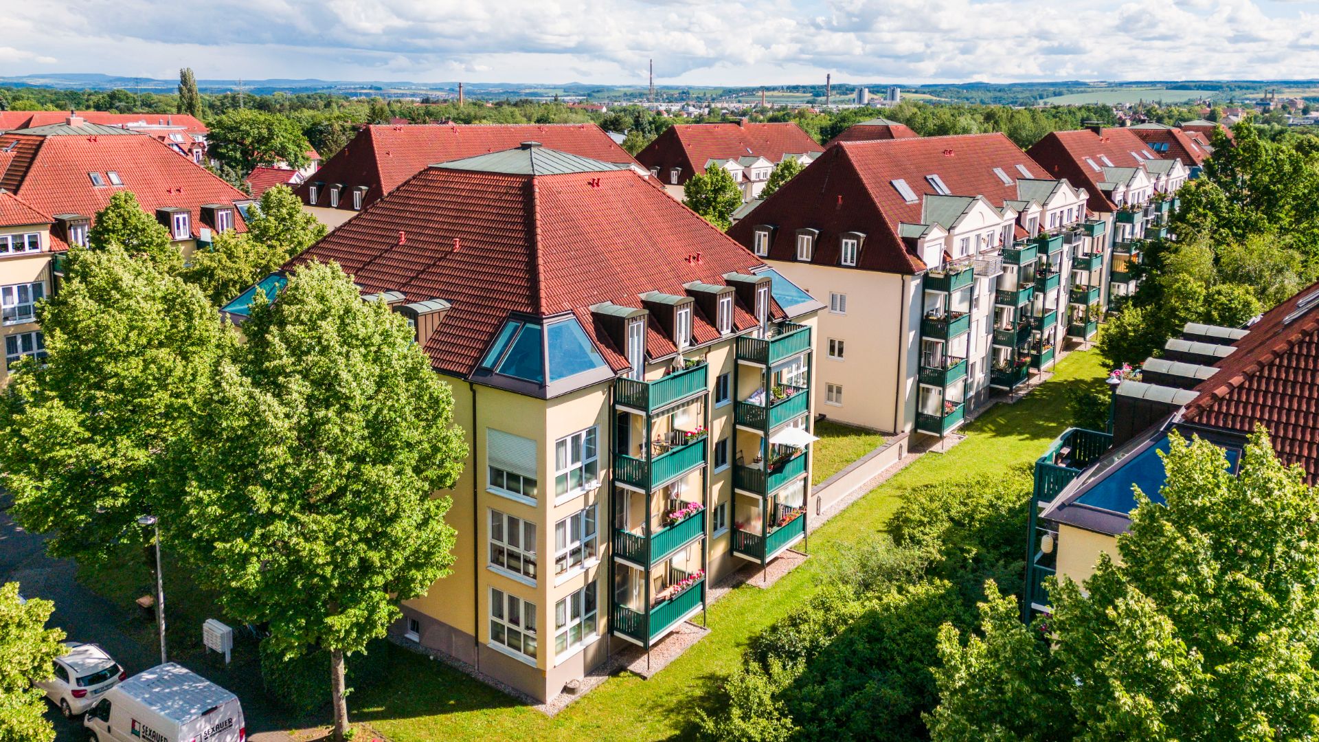 Mehrstöckige Wohngebäude mit roten Dächern und Balkonen, umgeben von Bäumen.