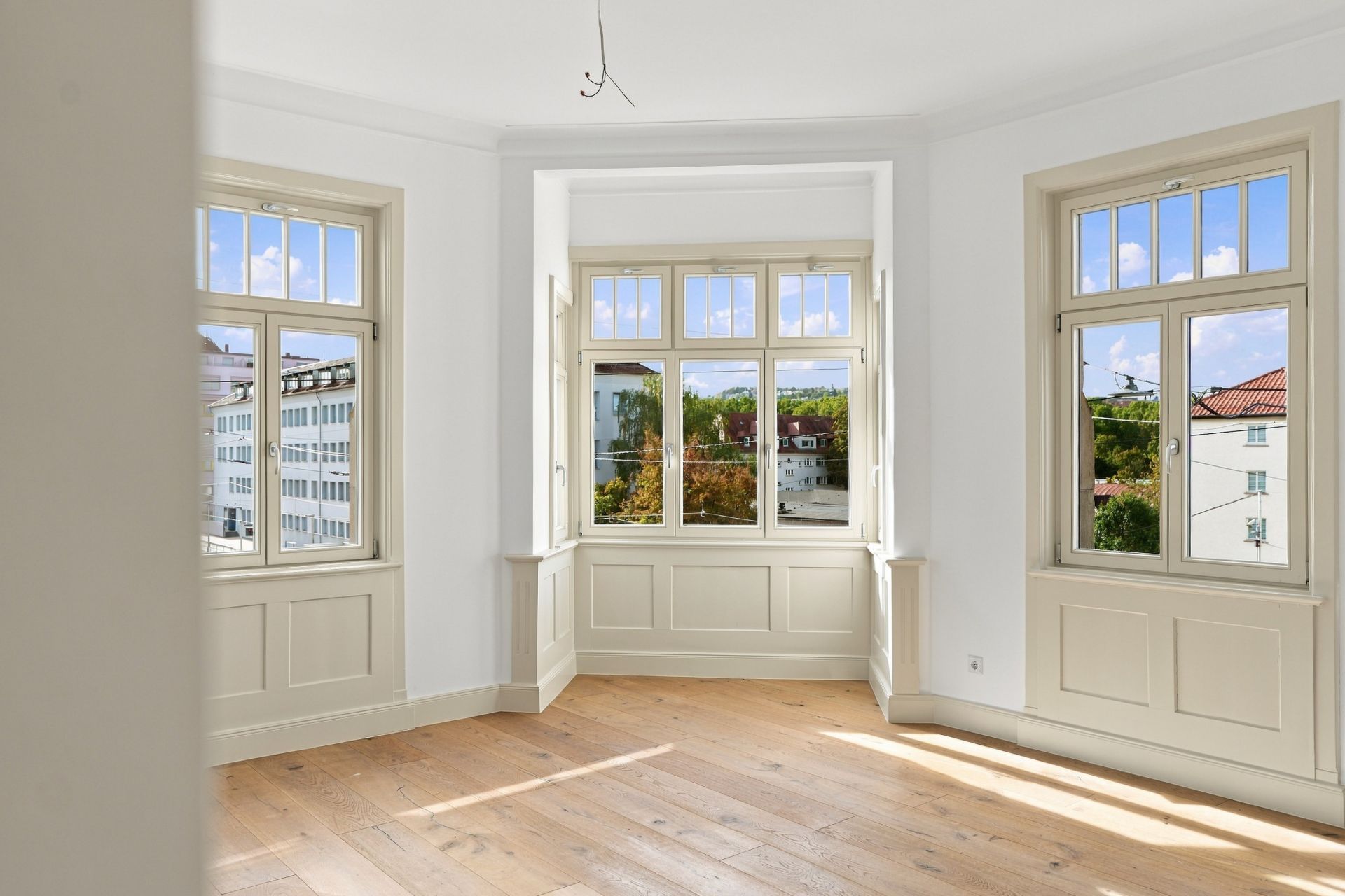 Heller leerer Raum mit drei großen Fenstern und Holzboden.