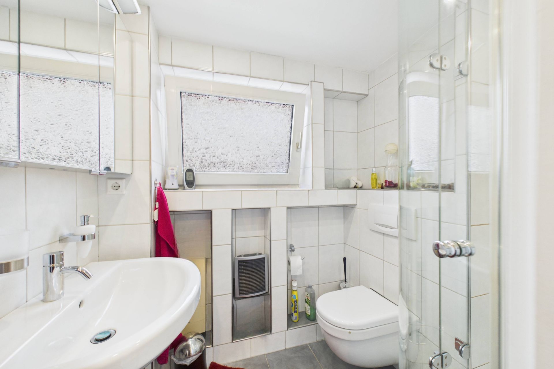 Helles Badezimmer mit Waschbecken, WC, Dusche und Fenster.