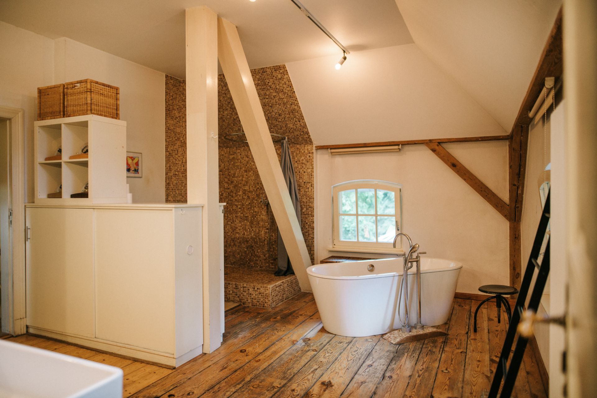 Helles Badezimmer mit freistehender Badewanne, Holzboden und offenen Regalen.