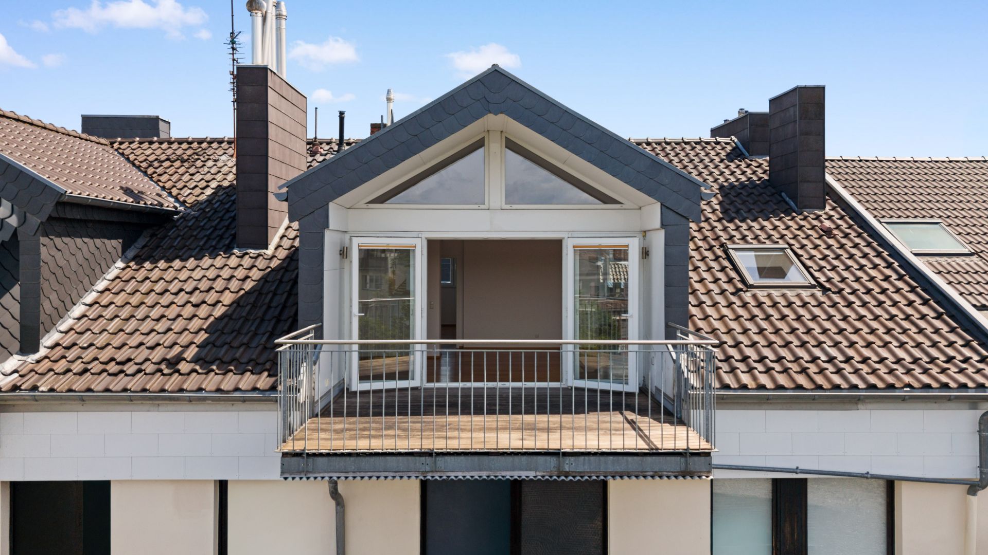 Balkon mit Doppeltüren und Dachfenster an einem Wohnhaus mit Ziegeldach.