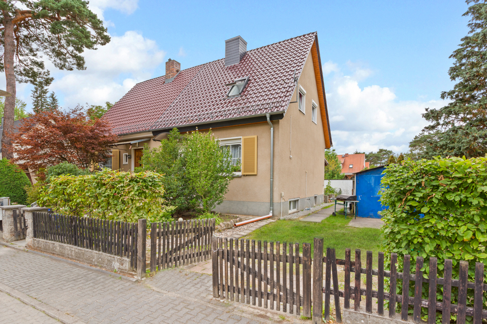 Einfamilienhaus mit Garten, Zaun und Schuppen, umgeben von Bäumen und Sträuchern.