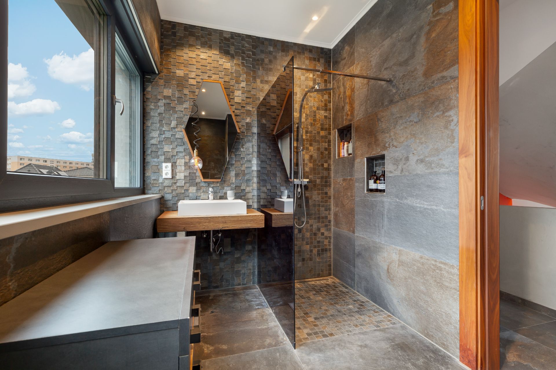 Modernes Bad mit begehbarer Dusche, großem Fenster, Waschbecken und Spiegel, Fliesen in Grau- und Brauntönen.