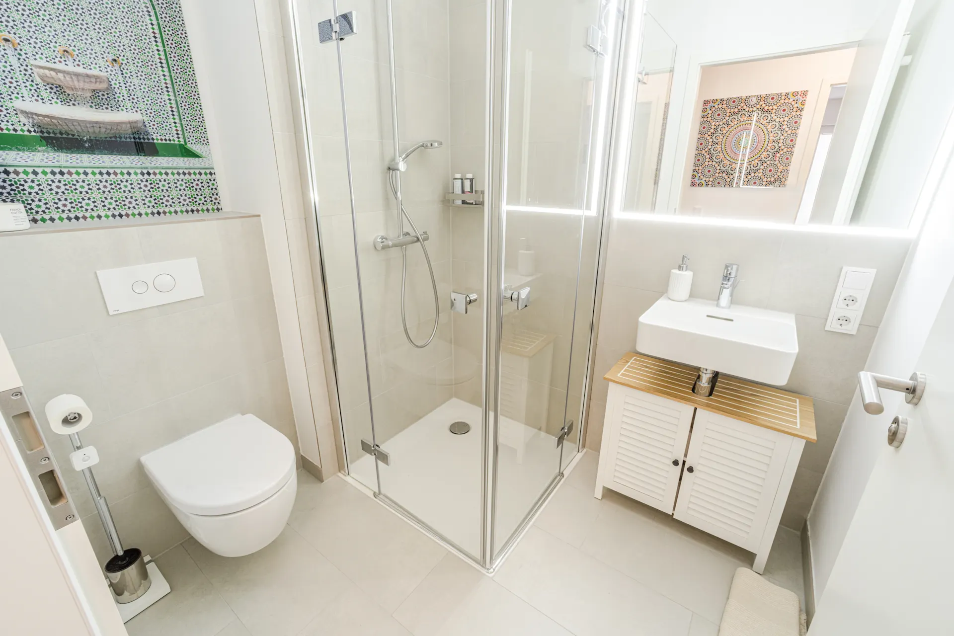 Modernes Bad mit Dusche, Toilette, Waschbecken und buntem Fliesenbild an der Wand.