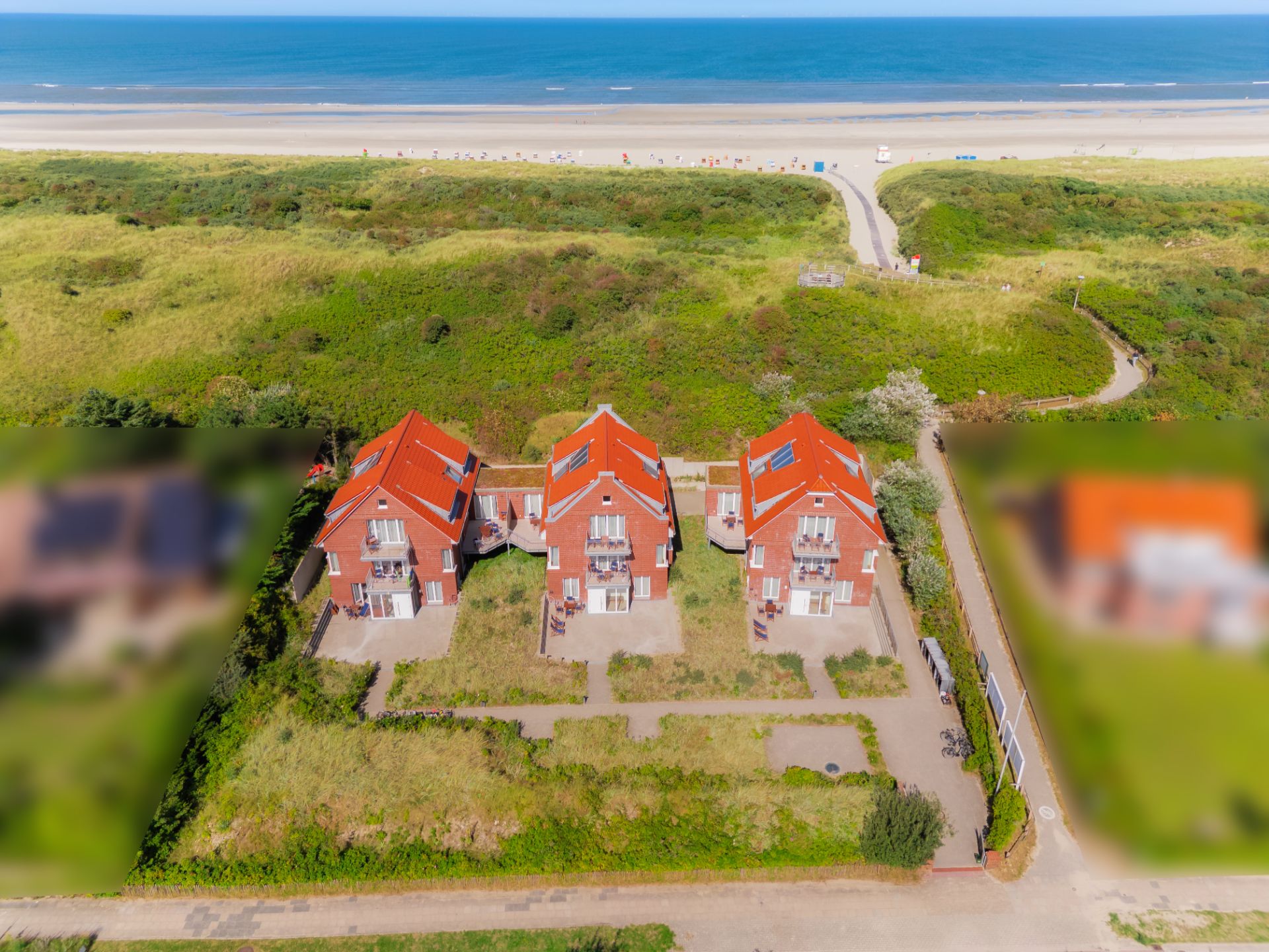 Drei rote Backsteinhäuser mit Gärten, nahe Dünen und Sandstrand, Luftaufnahme.