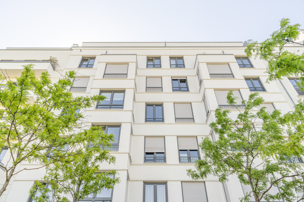 Mehrstöckiges Wohnhaus mit vielen Fenstern und grünen Bäumen davor.