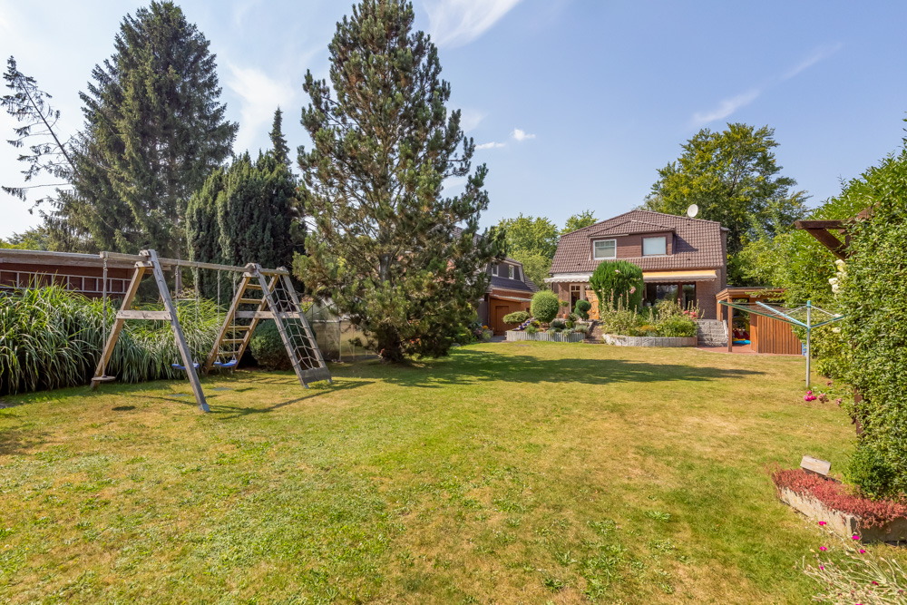 Garten mit Rasen, Bäumen, einer Kinderschaukel und Blick auf ein Einfamilienhaus.