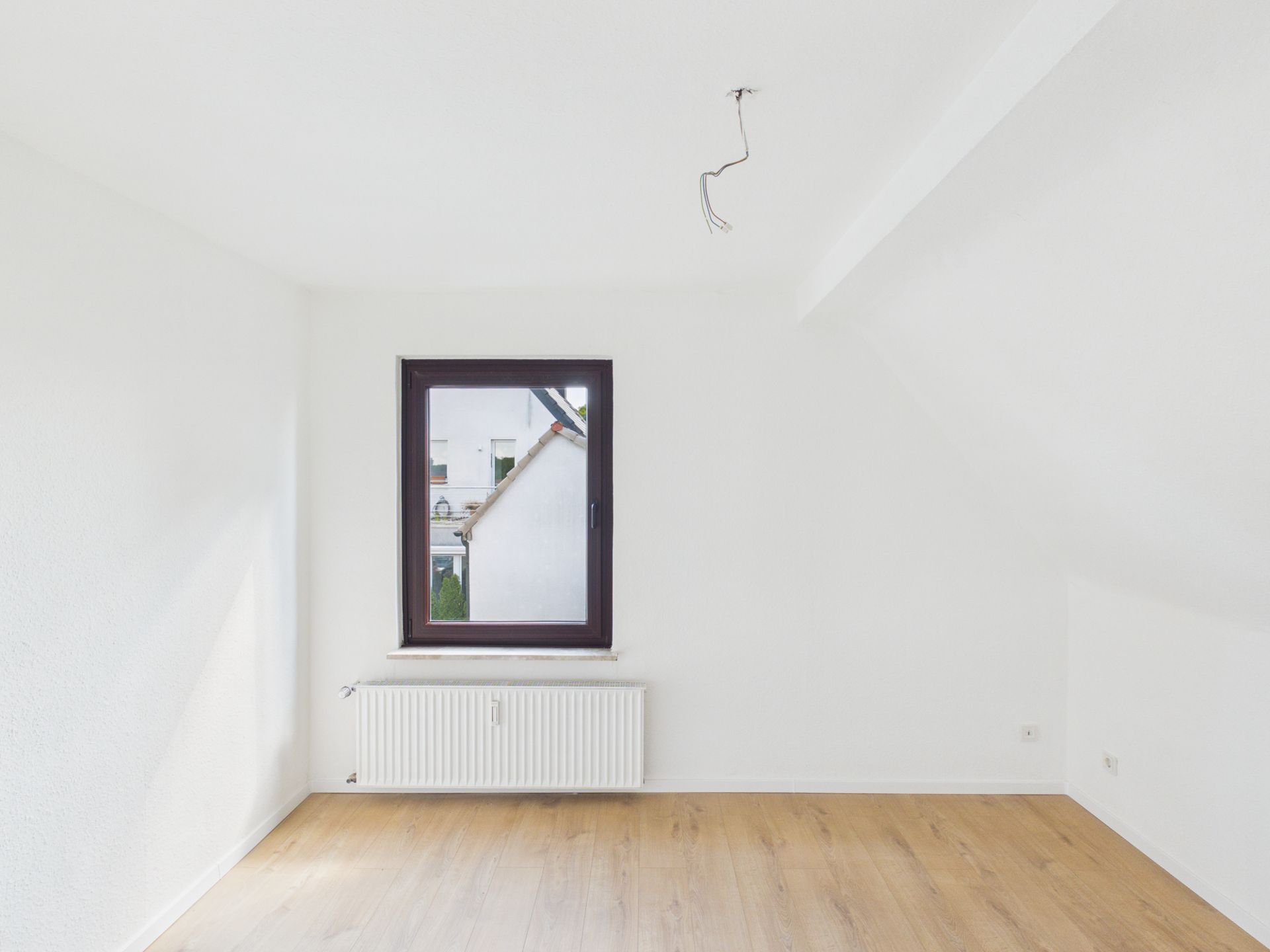 Leerer, weiß gestrichener Raum mit Holzfußboden und Fenster mit Blick nach draußen.