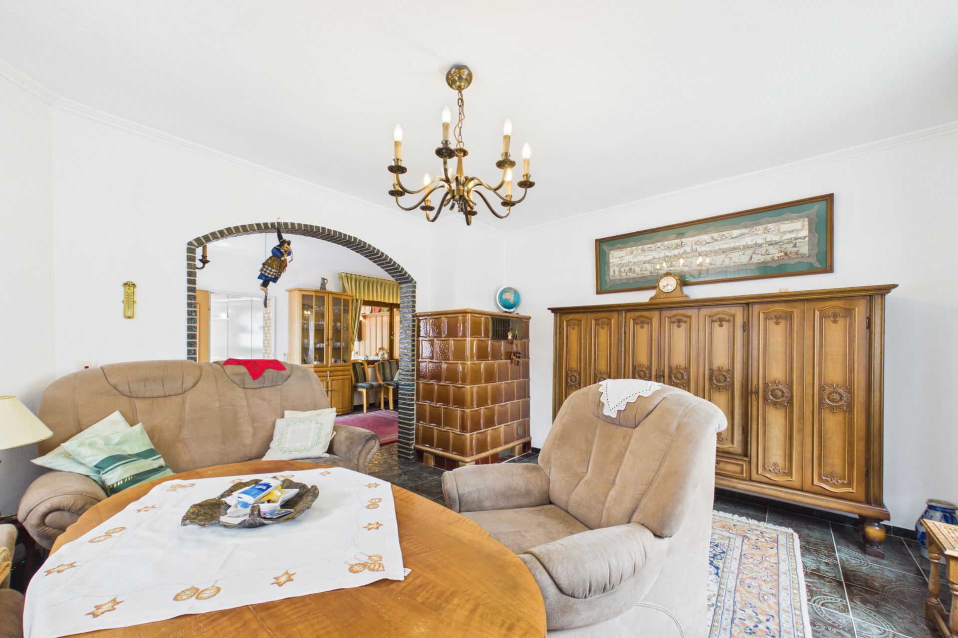 Wohnzimmer mit Polstermöbeln, Holztisch, Kronleuchter und großem Holzschrank.