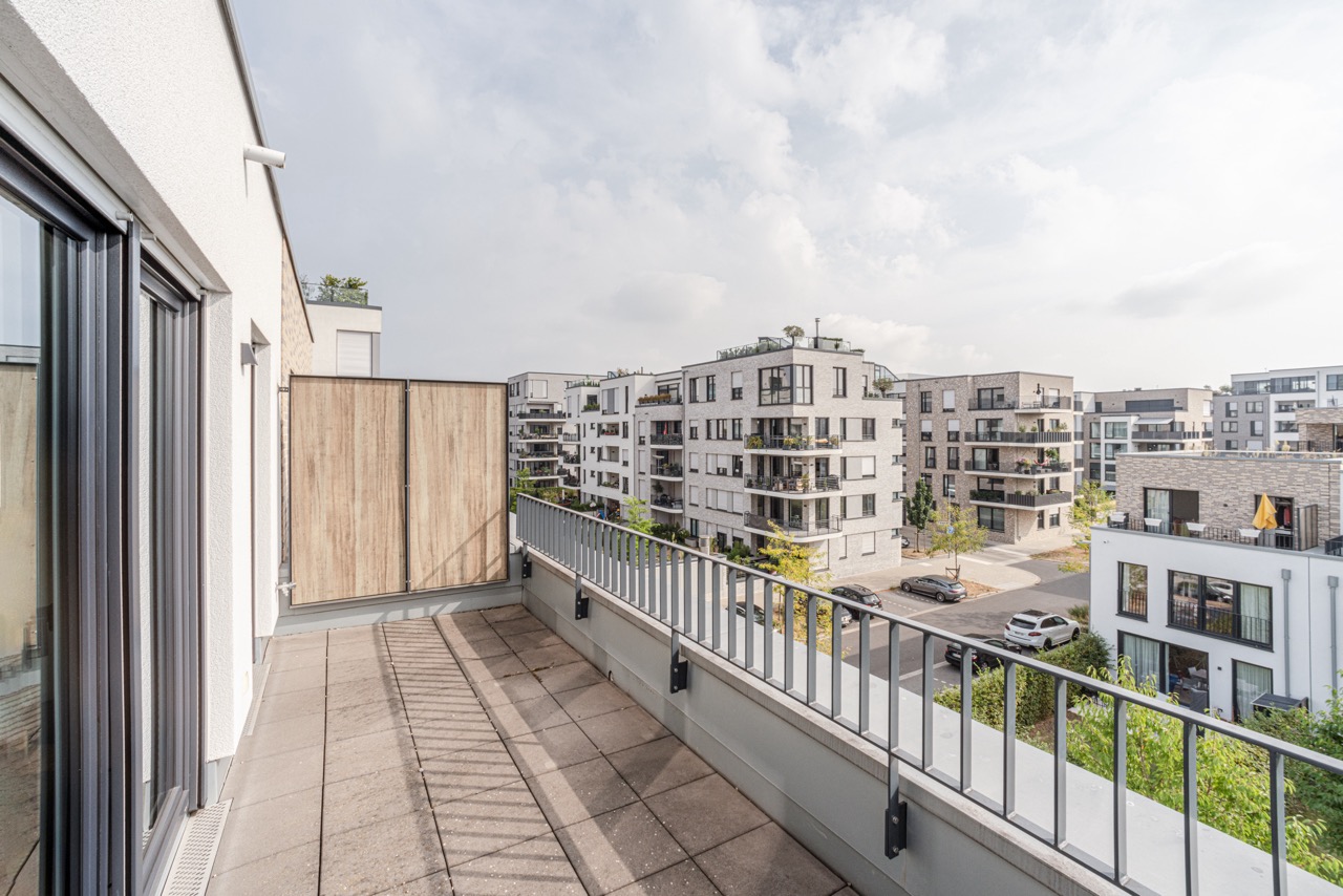 Großer Balkon mit Blick auf moderne Wohngebäude und eine ruhige Straße.