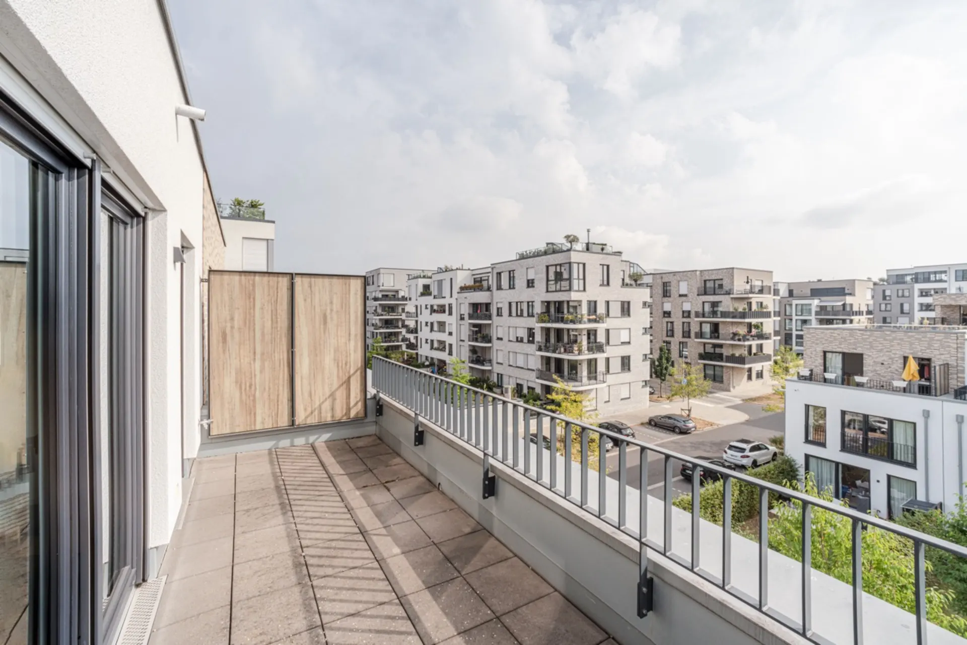 Großer Balkon mit Blick auf moderne Wohngebäude und eine ruhige Straße.