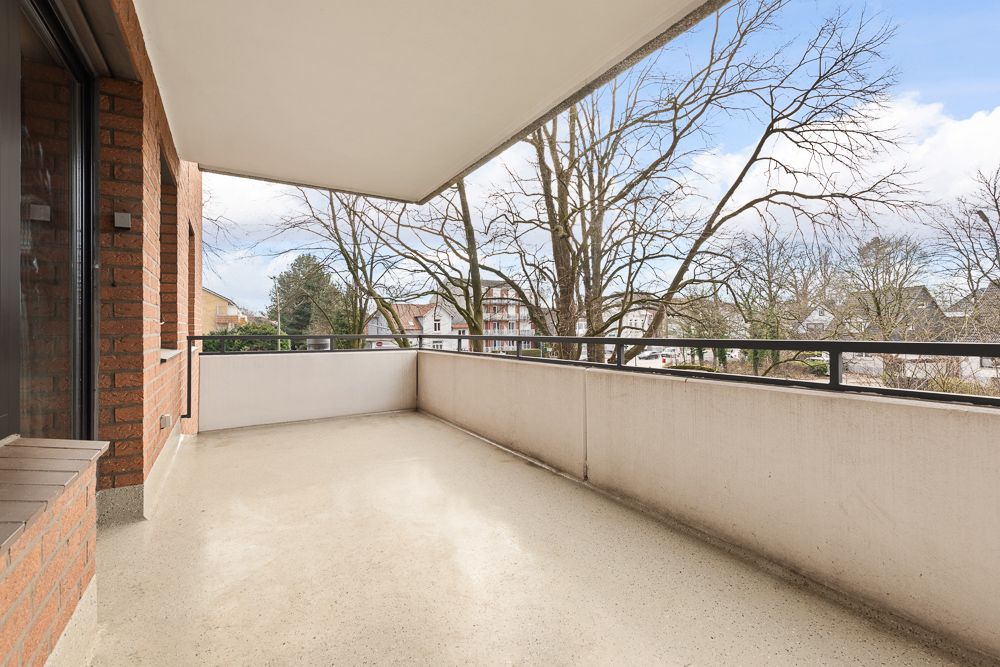 Großer Balkon mit Überdachung, Betonboden und Blick auf Bäume und Wohnhäuser.