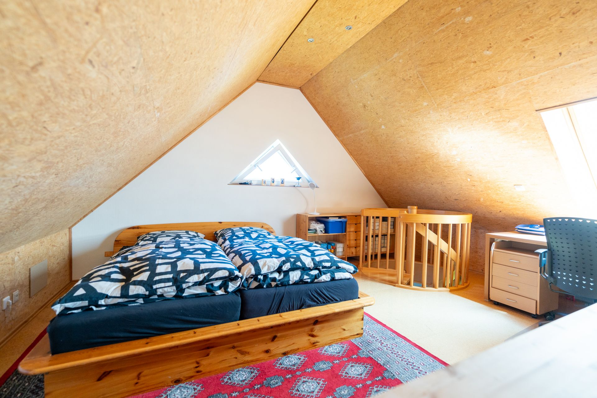 Gemütliches Dachzimmer mit Doppelbett, Schreibtisch, Stuhl und runder Treppe.