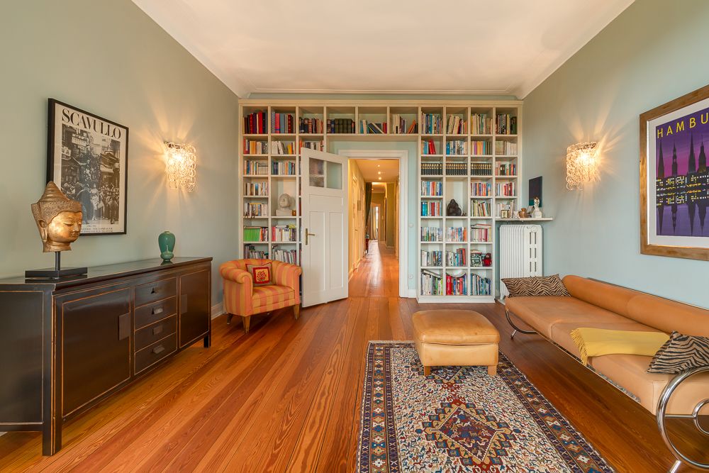Wohnzimmer mit Holzboden, Bücherregal, Ledersofa, Teppich und Wandbildern.