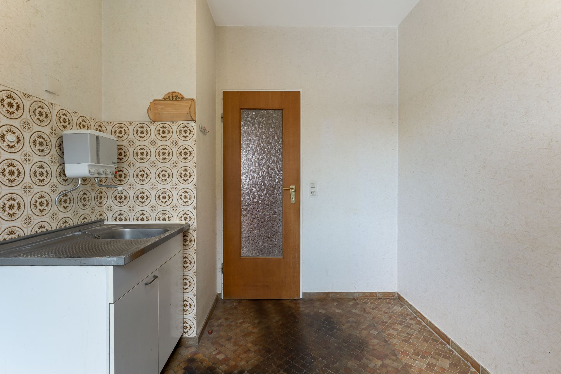 Kleine Küche mit Spülbecken, gemusterte Fliesenwand und Holztür.