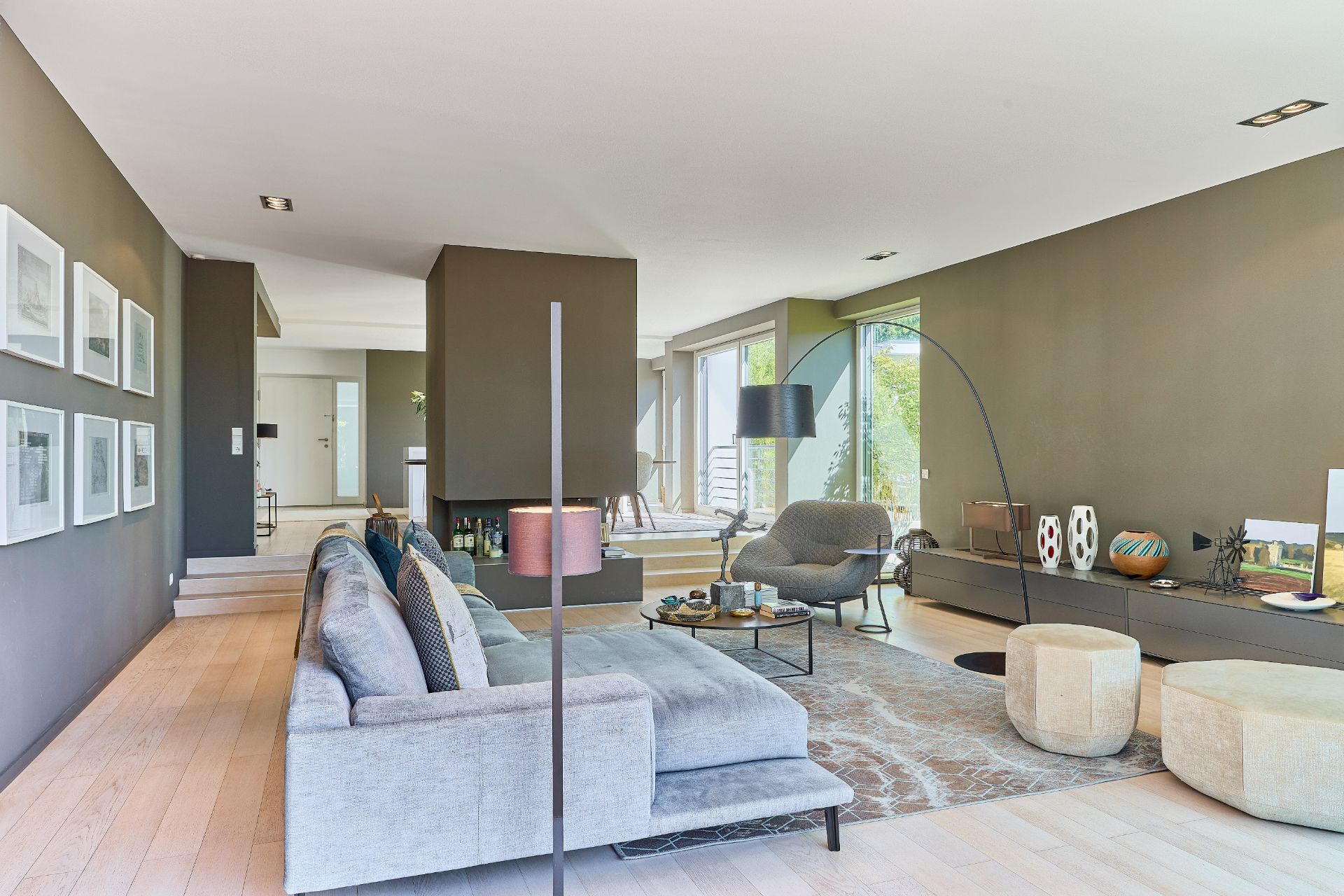 Modernes Wohnzimmer mit grauem Sofa, Sesseln, Couchtisch und großen Fenstern.