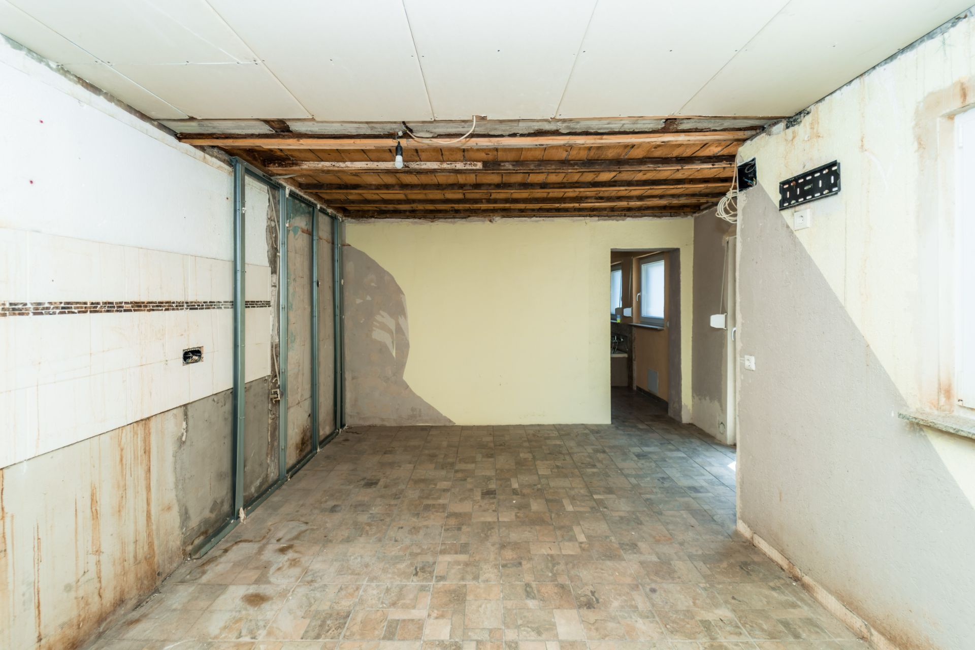 Leerer, renovierungsbedürftiger Raum mit sichtbarer Decke und gefliestem Boden.