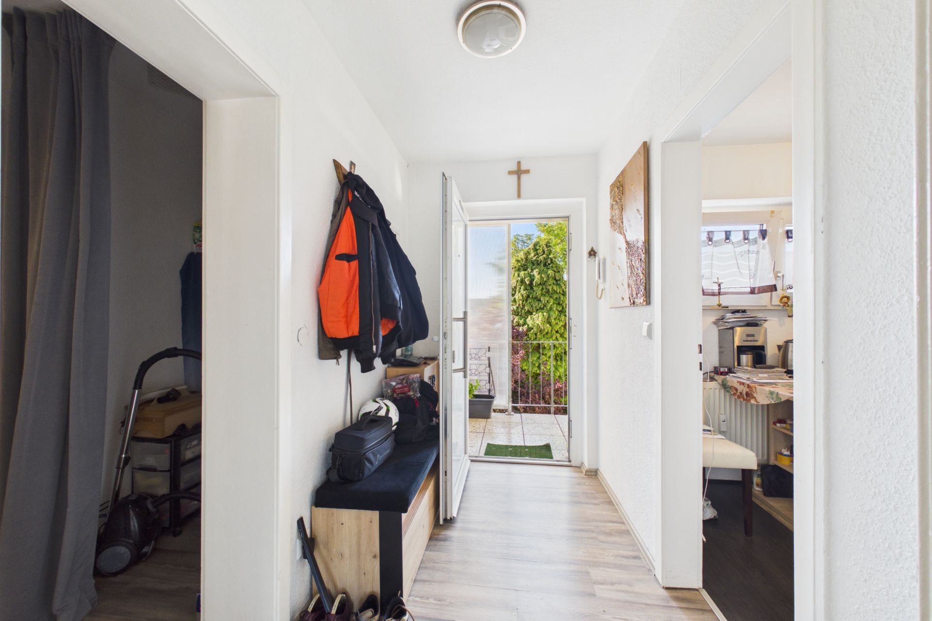 Heller Flur mit Garderobe, offenen Türen und Blick nach draußen auf Balkon mit grünem Baum.