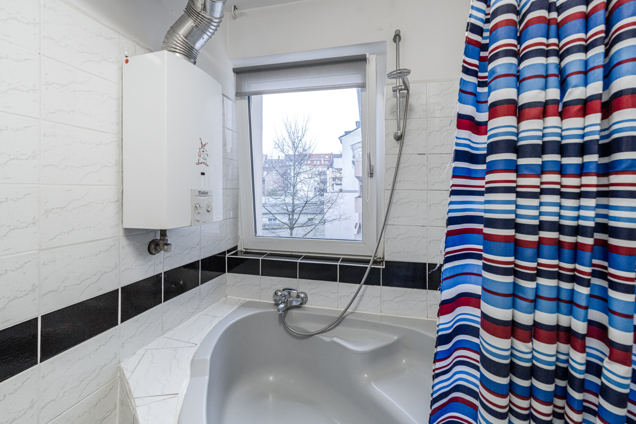 Badezimmer mit Eckbadewanne, Gastherme, Fenster und gestreiftem Duschvorhang.