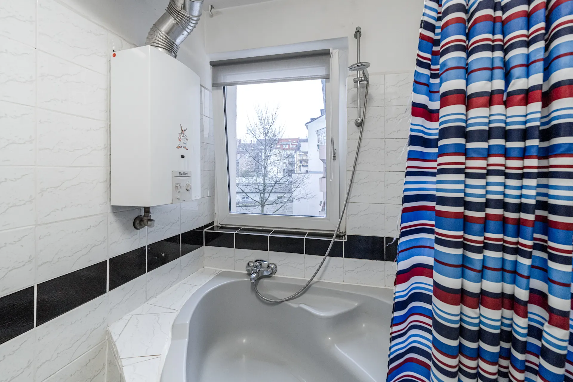 Badezimmer mit Eckbadewanne, Gastherme, Fenster und gestreiftem Duschvorhang.