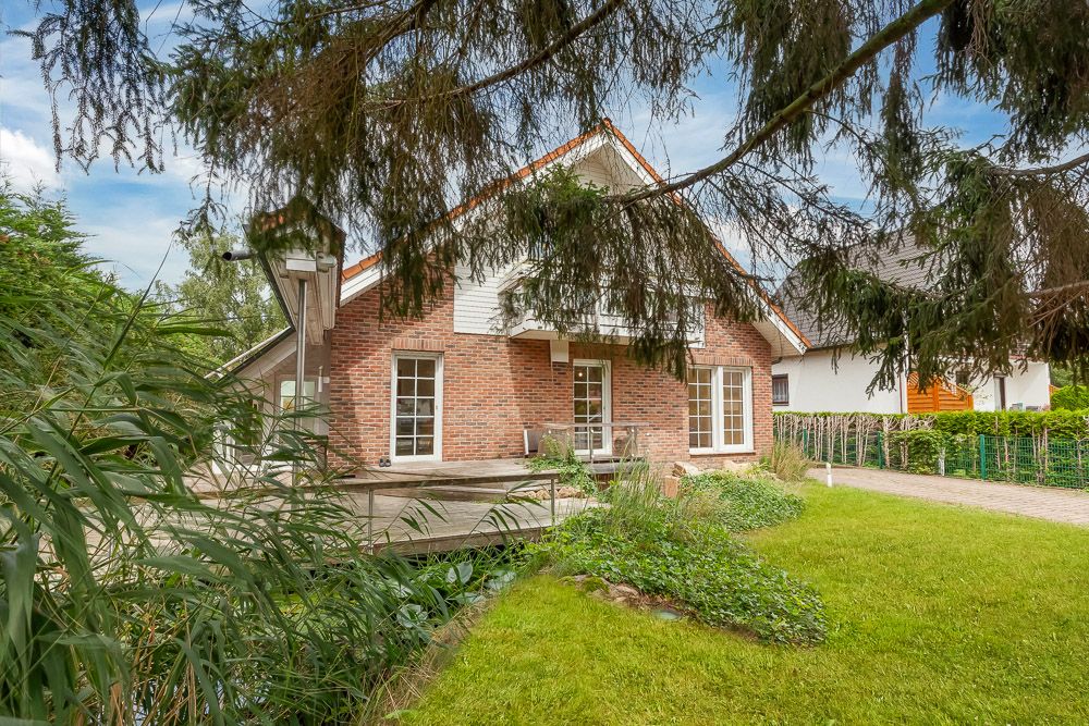 Backsteinwohnhaus mit Terrasse und Garten, umgeben von Bäumen und Sträuchern.